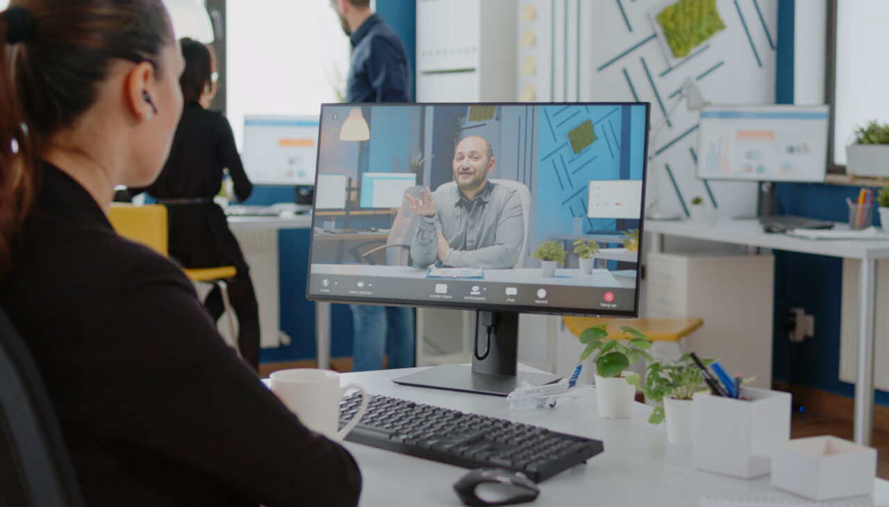 Picture of a woman sitting at her desk interviewing a man on her computer.