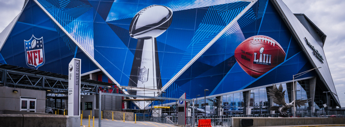 Image of the outside of a football stadium with the Super Bowl Trophy, NFL Logo and a football embedded over it.