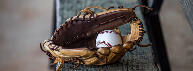 A baseball glove with a white baseball inside rests on a weathered wooden bench.