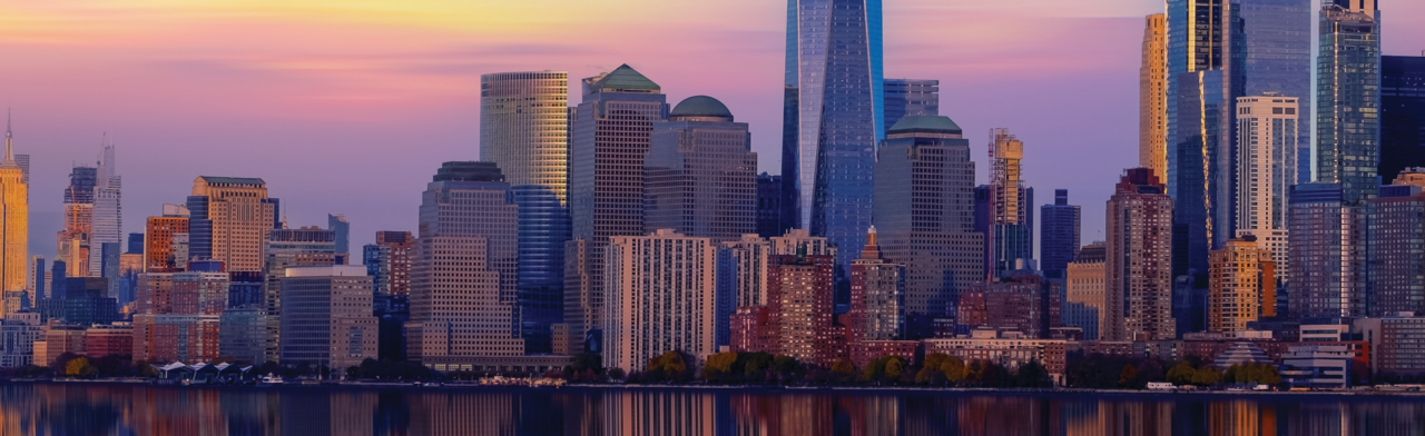 A panoramic view of the Manhattan skyline during a purple and orange sunset, featuring the One World Trade Center and surrounding skyscrapers reflected in the calm waters of the Hudson River.