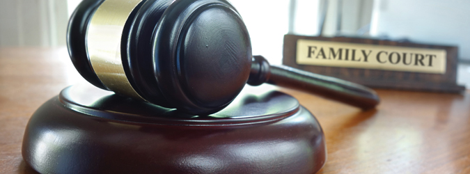 A judges gavel rests on a sound block, with a blurred sign reading FAMILY COURT in the background, symbolizing legal proceedings in family law.