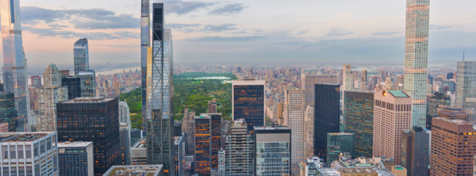 Aerial view of Manhattan skyscrapers with Central Park in the background under a partly cloudy sky at sunset.