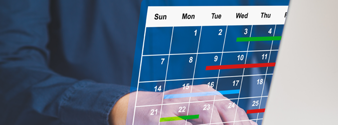A person uses a laptop behind a transparent digital calendar with color-coded events marked on different days of the month.
