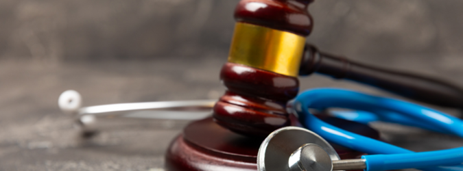 A judges gavel rests next to a blue stethoscope on a wooden surface, symbolizing the intersection of law and healthcare.