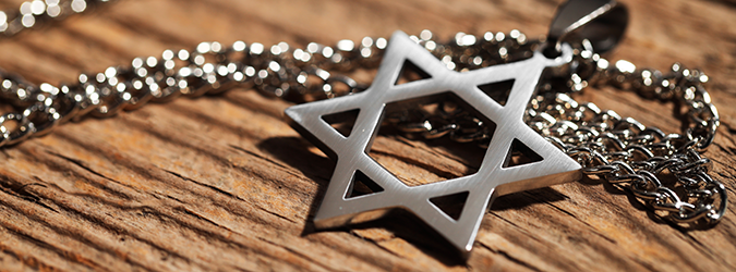 A silver Star of David pendant on a chain rests on a wooden surface, with sunlight highlighting the details of the metal.