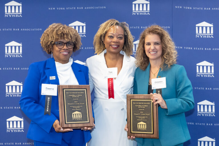 Three women in professional attire smile, holding awards in front of a blue backdrop with the New York State Bar Association logo. Two women each hold a plaque, and one woman in the center stands with them.