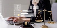 A person types on a laptop at a desk with a gavel and golden scales of justice. Legal icons and documents are digitally overlaid, suggesting law, legal advice, or online legal services.