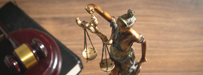 Bronze statue of Lady Justice holding scales, positioned next to a wooden gavel and a law book.