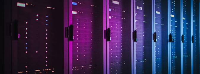 A row of server racks is illuminated by blue and purple LED lights in a dark data center.