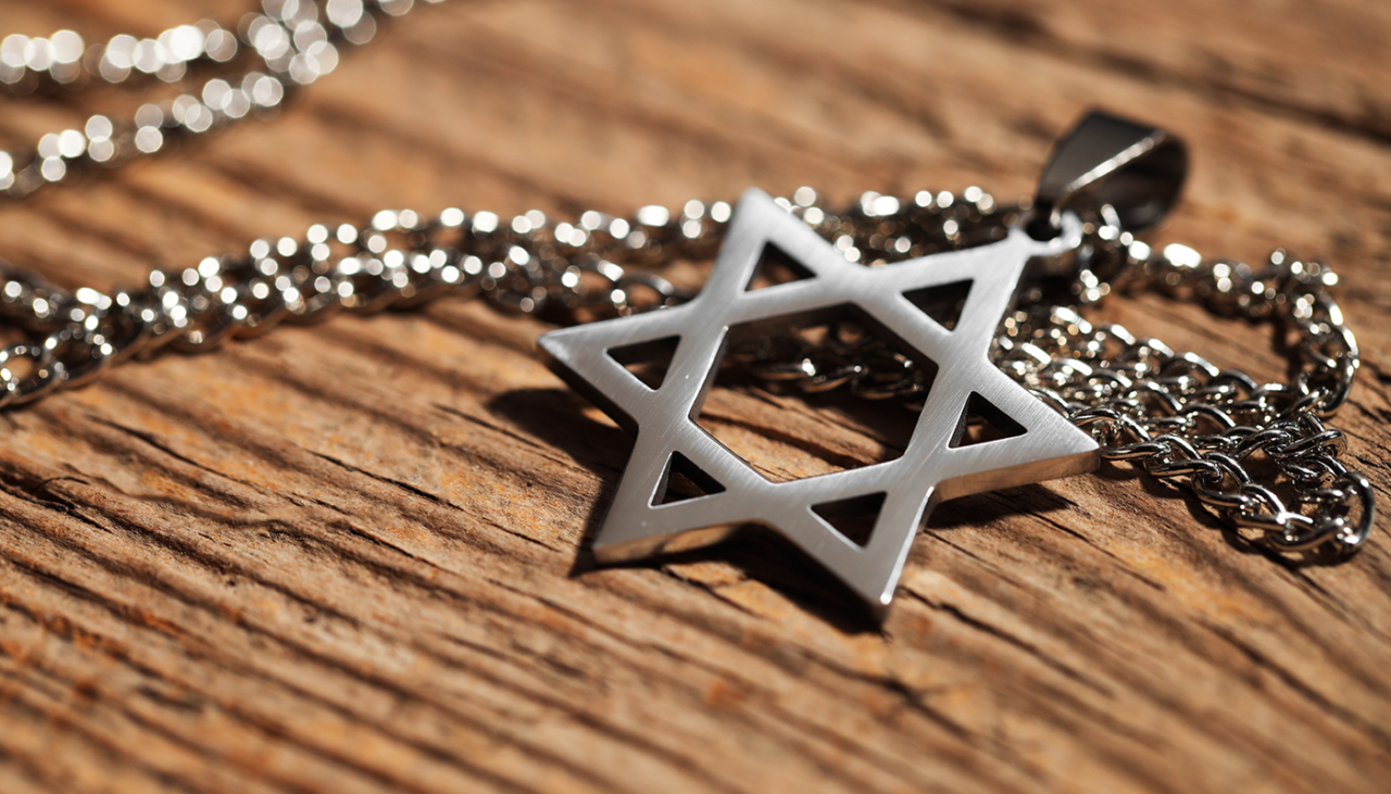 A silver-colored Star of David pendant on a chain resting on a wood surface.
