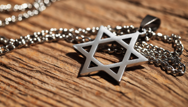 A silver-colored Star of David pendant on a chain resting on a wood surface.