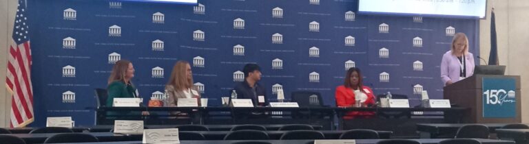 A panel of four speakers sits at a table on a stage in front of a blue backdrop with the New York State Bar Association logo, while a fifth person stands at a podium to the right beneath two large screens displaying the event title.
