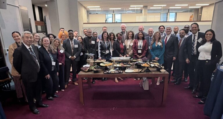 A large, diverse group of professionals posing for a photo behind a conference table filled with catered food.
