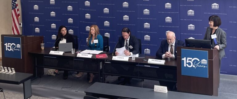 Five people seated at a panel table in front of a blue backdrop with the New York State Bar Association logo, as a speaker stands at a podium beneath two large screens displaying an event title.